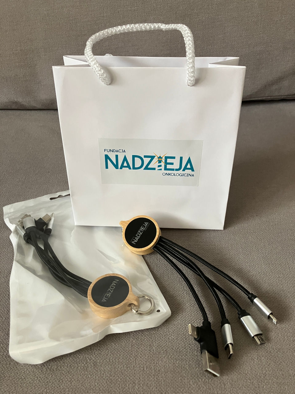 Zestaw gadżetów przygotowany przez Deuter DLM – biała torba papierowa Fundacji Nadzieja Onkologiczna z grubym sznurkiem oraz drewniany, okrągły hub USB z kilkoma typami złączy, zapakowane w ramach konfekcji